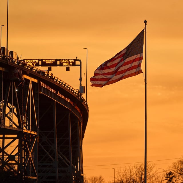 The sun sets behind the American and Canadian flags near the Blue Water Bridge border crossing between the two countries in Port Huron, Michigan, on April 3, 2025. Major US trade partners pilloried US President Donald Trump's global tariffs onslaught on April 3, but left the door open to negotiations as markets tumbled over fears his trade war would damage the world economy. (Photo by Geoff Robins / AFP) (Photo by GEOFF ROBINS/AFP via Getty Images)