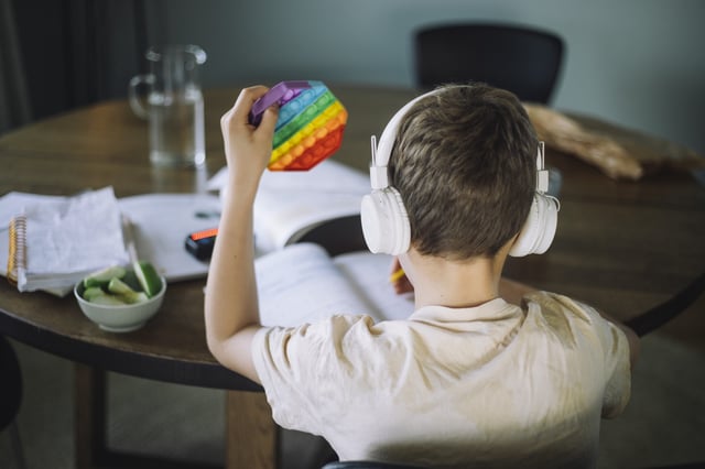 A child listens to music and plays with a push pop toy while doing homework.