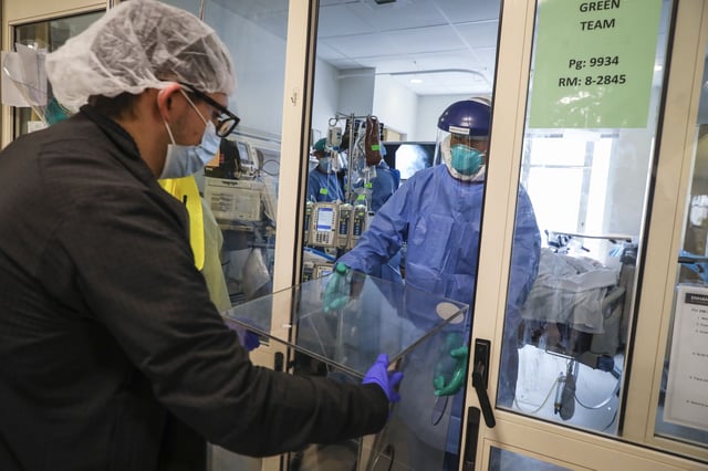MD Nicholas Flores, left, helps to remove a plastic protective box that  Dr. Bob Canelli, right, used to help perform a tracheostomy on a COVID-19 patient on the ICU floor at Boston Medical Center in Boston on April 30, 2020. Medical staff at BMC have had to adjust the way that they work and protect themselves in light of the coronavirus pandemic that has shook the country. (Photo by Erin Clark/The Boston Globe via Getty Images)