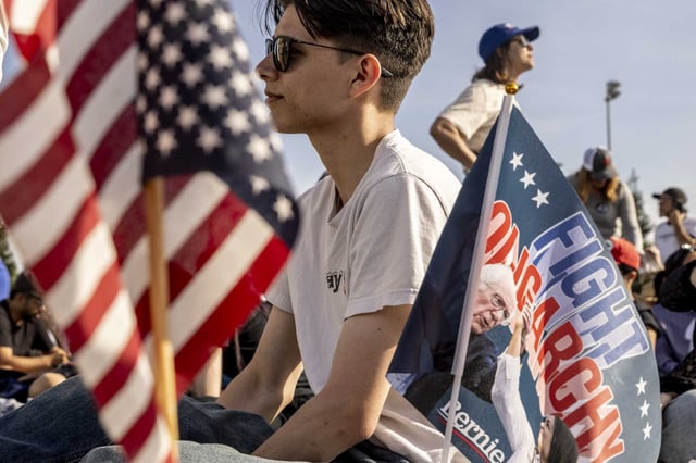 Ethan Jackline sits next to a flag planted by a friend as they attend a rally with Sen. Bernie Sanders and Rep. Alexandria Ocasio-Cortez in Folsom on April 15, 2025.