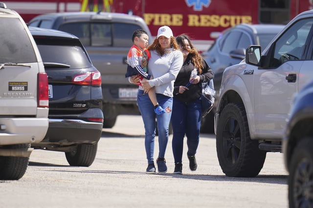 A woman carries a child as she and a student of Wilmer-Hutchins High School leave campus following reports of a shooting, in Dallas, Tuesday, April 15, 2025.