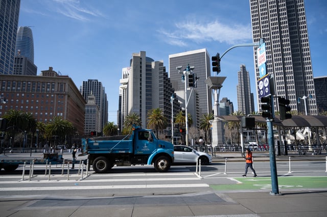 Blue utility truck passing through a crosswalk with palm trees and skyscrapers in the background near the Embarcadero, San Francisco, California, February 21, 2025.