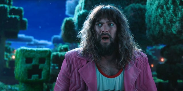 Jason Momoa as Garrett looking frightened as a Creeper lurks behind him in A Minecraft Movie.