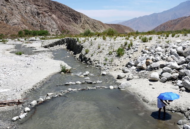 FILE: A child cools off underneath an umbrella at the Whitewater River on July 12, 2022, in Whitewater, Calif.