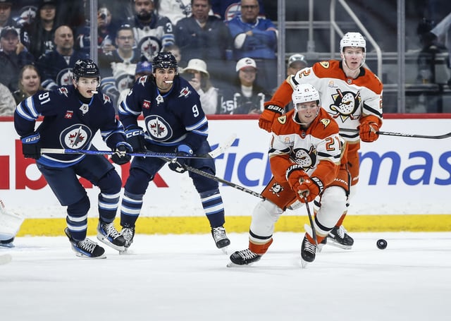 Anaheim Ducks' Isac Lundestrom (21) clears the puck as Winnipeg Jets' Cole Perfetti (91) and Alex Iafallo (9) look on during first period NHL action in Winnipeg on Wednesday, April 16, 2025. THE CANADIAN PRESS/John Woods