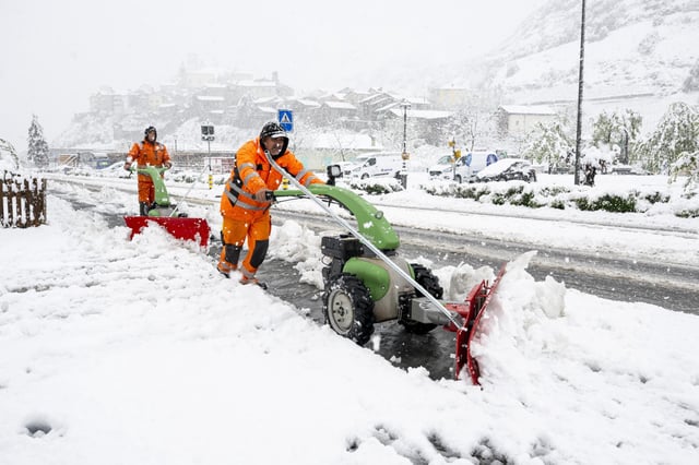 17.04.2025, Schweiz, Saillon: Zwei Personen räumen den Schnee auf der Straße weg. Aufgrund der starken Niederschläge gilt im Wallis die höchste Unwetter-Gefahrenstufe. Foto: Jean-Christophe Bott/KEYSTONE/dpa +++ dpa-Bildfunk +++