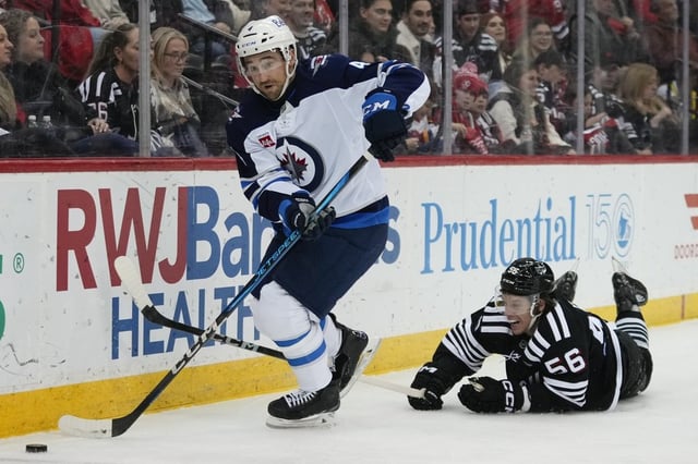 New Jersey Devils' Brenden Dillon (5) fights for control of the puck with Winnipeg Jets' Neal Pionk (4) during the second period of an NHL hockey game Friday, March 7, 2025, in Newark, N.J. (AP Photo/Frank Franklin II)