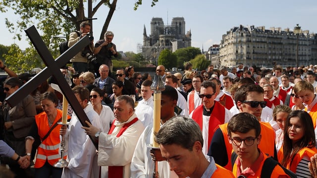 With Notre Dame cathedral in background, religious officials carry the cross during the Good Friday procession, Friday, April 19, 2019 in Paris. 
