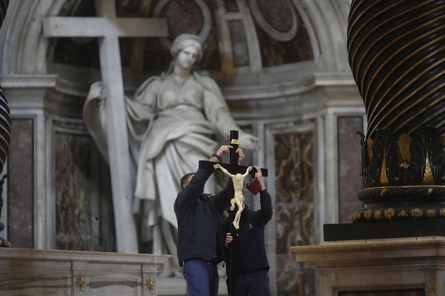 Workers place a crucifix on the altar of St. Peter's Basilica at the Vatican during the preparations for the celebration of the passion of Christ, Friday, April 18, 2025.