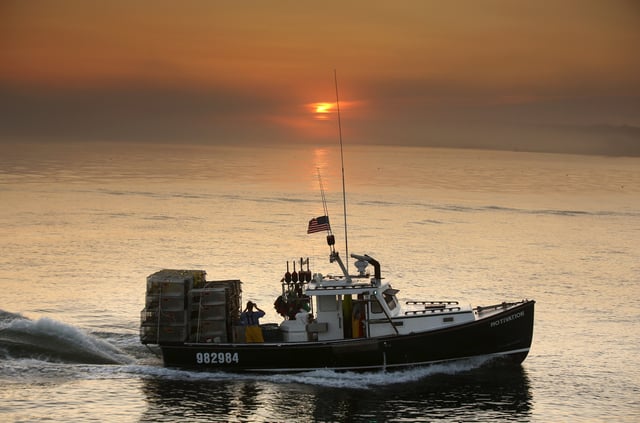 FILE - In this July 27, 2018, file photo, a sternman on a lobster fishing boat photographs the sunrise on the way out of Portland Harbor off South Portland, Maine. (AP Photo/Robert F. Bukaty, File)