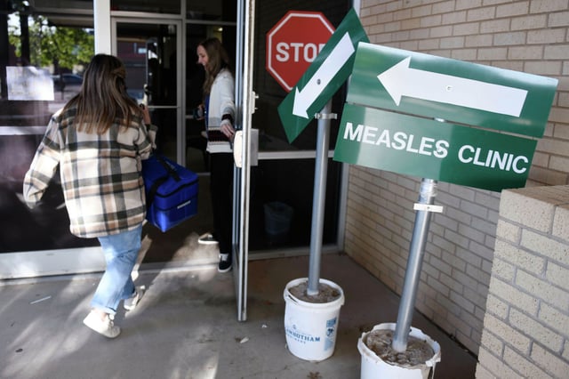 Health department staff members enter the Andrews County Health Department measles clinic carrying doses of the measles, mumps and rubella vaccine, Tuesday, April 8, 2025, in Andrews, Texas. 