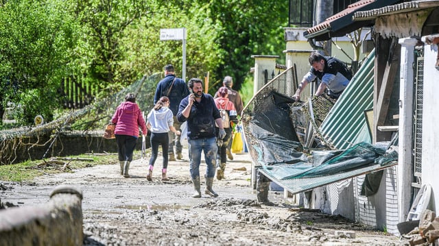 Menschen auf einer mit Schlamm bedeckten Straße vor einem zerstörten Haus in Lauriano, Region Piermont.