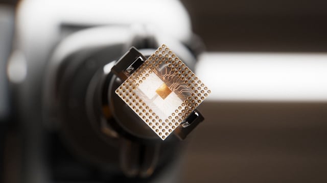An automated robotic arm is gripping a CPU inside of a circuit board factory. Part of a series images of semiconductors and microchips being installed by robots on a mother board. Conceptual 3D designed computer graphics.