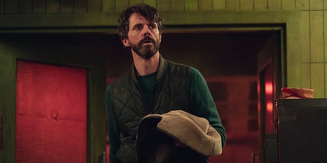 Matthew Goode holding his jacket in front of doors in Dept. Q