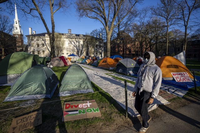 FILE - A student protester against the war in Gaza walks past tents and banners in an encampment in Harvard Yard, at Harvard University in Cambridge, Mass., on April 25, 2024. (AP Photo/Ben Curtis, file)