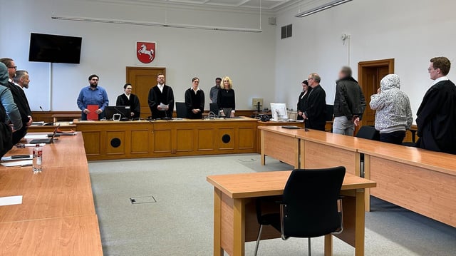 Mehrere Angeklagte stehen in einem Gerichtssaal.