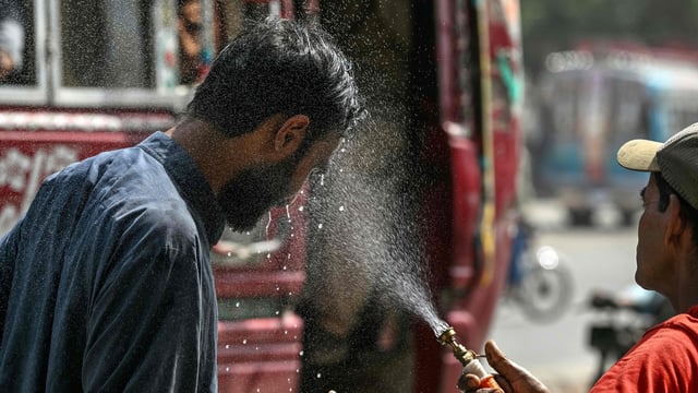 A volunteer of the Edhi Foundation sprays water on a passerby's face to cool off on a hot summer day along a road amid the ongoing heatwave in Karachi on April 21, 2025. (Photo by Asif HASSAN / AFP)