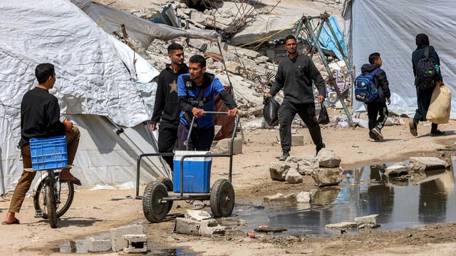 Menschen transportieren Wasserkanister in der Nähe der Trümmer eines eingestürzten Gebäudes im Westen von Gaza-Stadt.