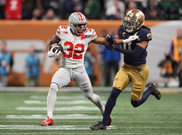 Ohio State Buckeyes running back TreVeyon Henderson (32) stiff arms Notre Dame Fighting Irish safety Xavier Watts (0) in the first half in the CFP National Championship college football game at Mercedes-Benz Stadium.