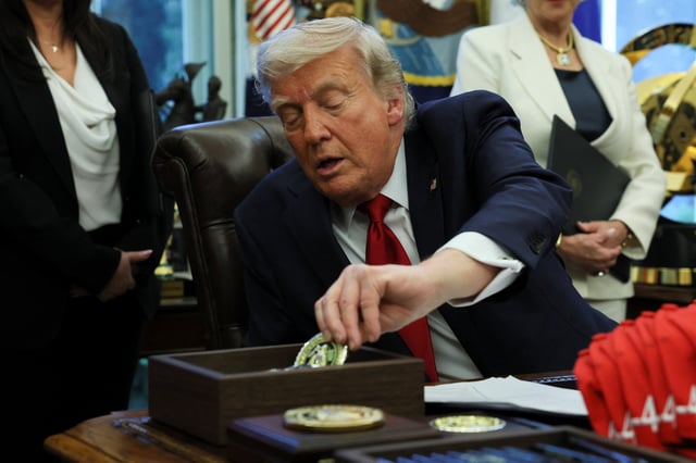 U.S. President Donald Trump picks up a challenge coin to hand to veterans during an executive orders signing event in the Oval Office at the White House in Washington, D.C., U.S., April 23, 2025. REUTERS/Leah Millis