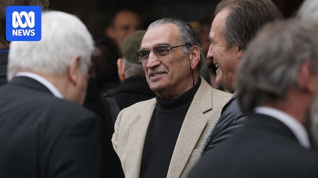 An older man in tinted glasses among a crowd of people.