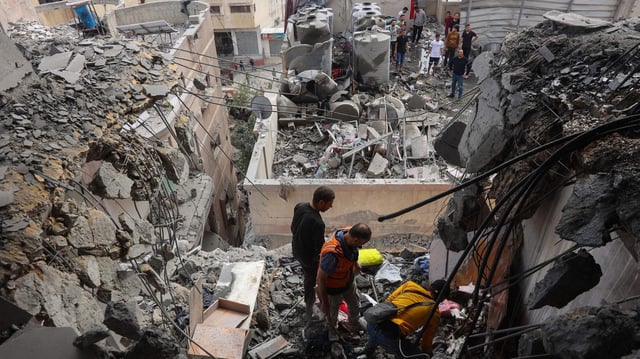 Menschen stehen in Trümmern eines zerstörten Gebäudes im Gazastreifen