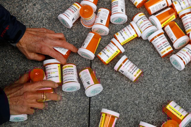In this 2019 photo, a protester gathers containers that look like OxyContin bottles at an anti-opioid demonstration in front of the US Department of Health and Human Services headquarters in Washington, DC.