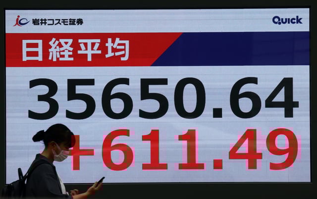 A woman walks in front of big screen displaying Japan's Nikkei share average outside a brokerage in Tokyo, Japan April 25, 2025. REUTERS/Issei Kato