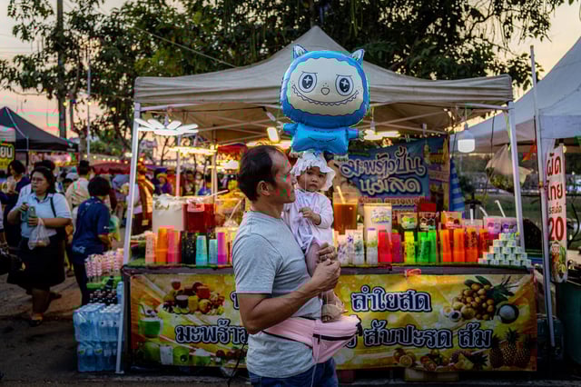 A man carries his baby and a balloon of one of the monsters, through a local carnival on February 7, 2025 in Udon Thani, Thailand.