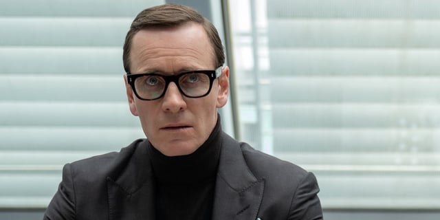 Michael Fassbender as George Woodhouse in glasses sitting down while looking up in Black Bag