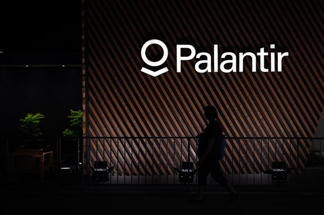 A woman walks under a sign of big data analytics US software company Palantir in Davos on May 22, 2022.