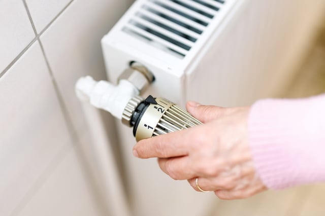 Eine Frau stellt an einem Thermostaten die Temperatur von einem Heizkörper ein.