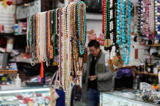 Lyndon Lin, owner C.K. Color Stone and Beads, rear, walks behind beads from China and other Asian countries displayed at his shop in Chinatown in San Francisco, Friday, April 18, 2025. (AP Photo/Jeff Chiu)