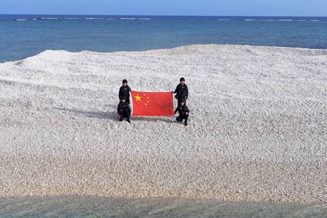 Chinese coast guard offices display their national flag on a tiny sandbar in the disputed Sandy Cay in April, 2025.