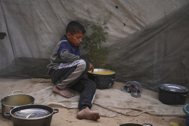 Mohammad Abu Zeid, 12, tastes the food prepared for a meal in his family tent in Muwasi, on the outskirts of Khan Younis in the southern Gaza Strip, Thursday, April 24, 2025. (AP Photo/Abdel Kareem Hana)