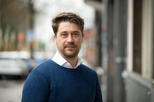 Der Bremer AfD-Vorsitzende Sergej Minich trägt einen blauen Pullover und darunter ein weißes Hemd, er schaut freundlich in die Kamera – die AfD hat in Bremen eine Höchstumfragewert erreicht