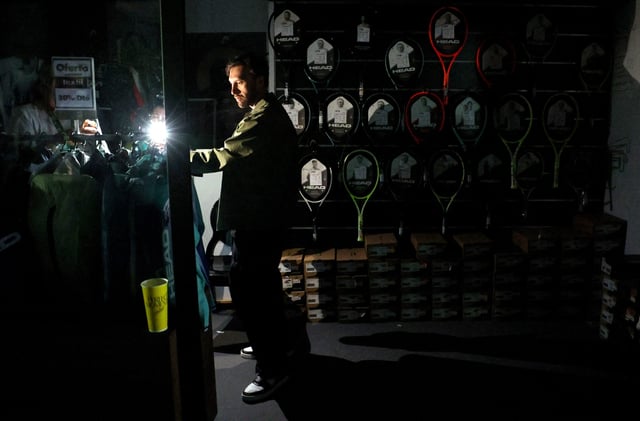 Tennis - Madrid Open - Park Manzanares, Madrid, Spain - April 28, 2025 A man uses his cell phone's flashlight in a dark sports shop after the matches get suspended due to a power outage REUTERS/Violeta Santos Moura