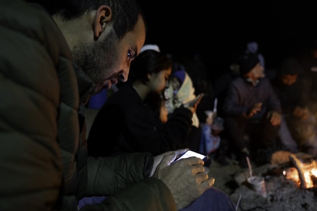 An immigrant from Afghanistan checks messages while connected to satellite WIFI at a humanitarian aid camp next to the U.S.-Mexico border on January 19, 2025 near Sasabe, Arizona.