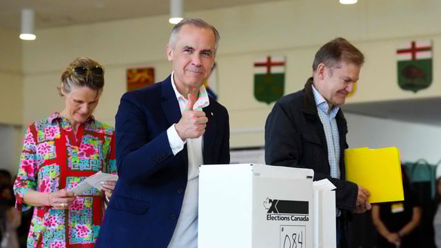 Canadian Prime Minister and Liberal leader Mark Carney, alongside his wife Diana Fox Carney (L), gives a thumbs up after casting his ballot a polling station during the federal election in Ottawa.