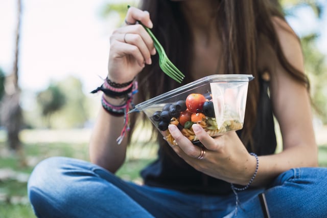 Young woman sitting in a park, eating salad