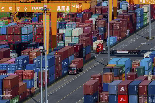 Trucks move amid containers stacked at a container terminal port on the Yangtze River in southwest China's Chongqing Municipality.