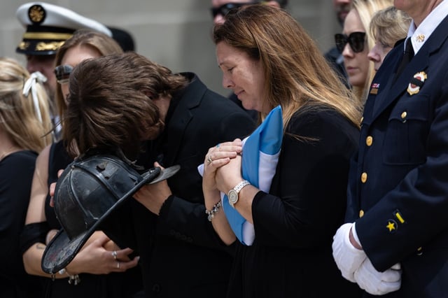 Michael Meyer, left, buries his head into his father’s Chicago Fire Department helmet, next to his mother, Kristen Meyer, during the funeral service of Capt. David Meyer on April 29, 2025, at St. John Brebeuf Church in Niles. (Audrey Richardson/Chicago Tribune)