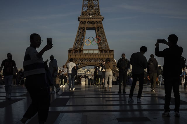 FILE - People use their smartphones near the Olympic rings that are displayed on the Eiffel Tower in Paris, June 7, 2024 in Paris. (AP Photo/Aurelien Morissard, File)