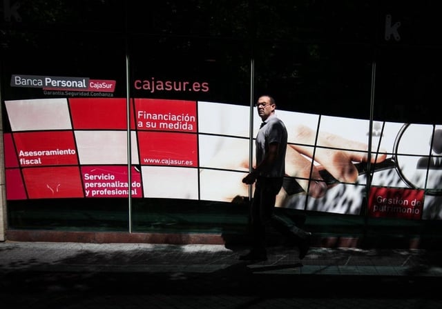 Un viandante pasa por un panel promocional de Cajasur en una de sus sedes en Córdoba