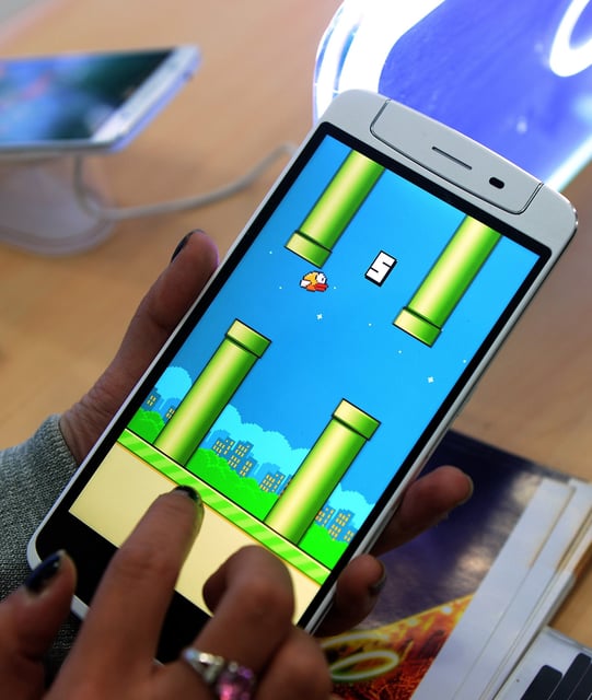 FILE - An employee plays the game Flappy Bird at a smartphone store in Hanoi on February 10, 2014. The game was incredibly popular after being launched in 2013, but was taken down the next year.