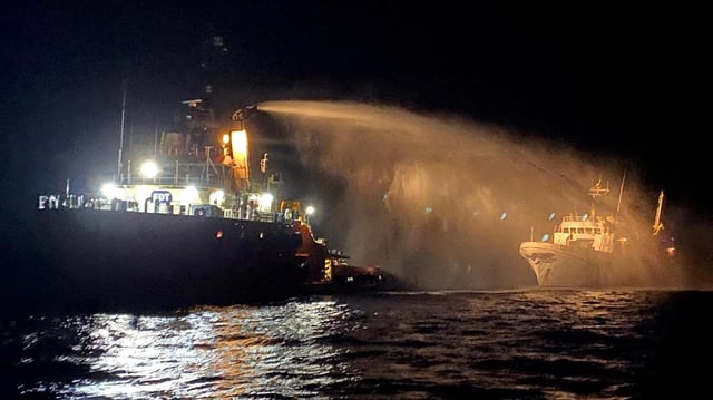Ein Schlepper löscht nachts ein Feuer auf einem Schiff.