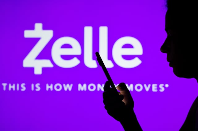 In this photo illustration the Zelle logo seen in the background of a silhouetted woman holding a mobile phone.