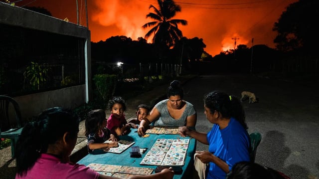 Neighbors play board games under a sky lit by gas flares near Punta de Mata in eastern Venezuela on Nov. 5, 2022. Oil producing countries are bracing for a bumpy ride this year, with a precipitous drop in prices to the lowest levels in four years seen as the initial, alarming sign of looming turmoil.