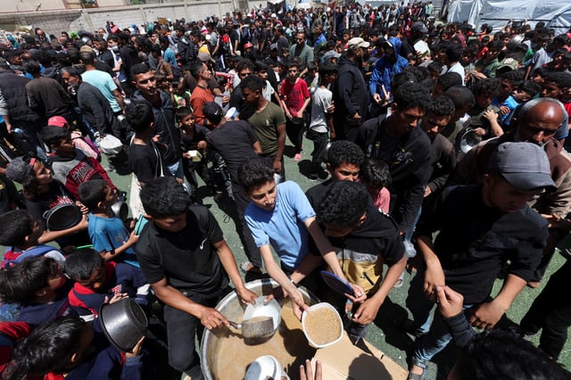 Palestinians wait to receive food cooked by a charity kitchen, in Nuseirat, central Gaza Strip, April 28, 2025. REUTERS/Ramadan Abed/File Photo