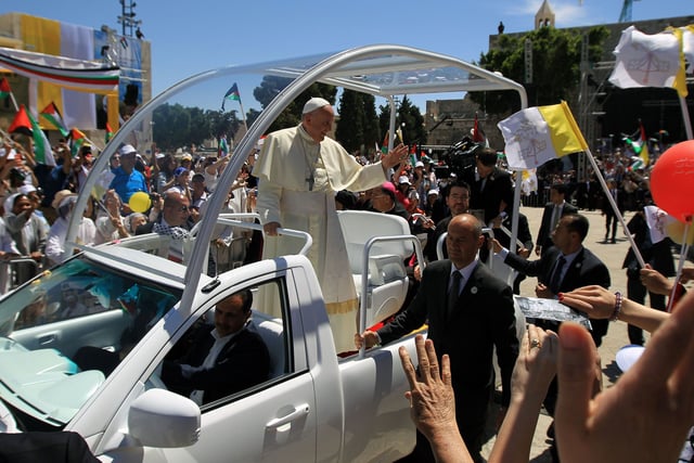 Pope Francis waves to the crowd, from his popemobile, as he arrives at the Manger Square before presiding over an open-air mass on May 25, 2014, outside the Church of the Nativity in Bethlehem, West Bank. Pope Francis arrived in Bethlehem to begin the most sensitive part of his three-day Middle East tour aimed at forging regional peace and easing an age-old rift within Christianity.